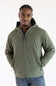 A man wearing a dusty olive green hooded Carhartt jacket paired with blue jeans, posed against a plain white background with hands in his pockets.