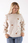 A smiling blond woman wearing a beige fleece crewneck sweatshirt with an all-over embroidered gingerbread man pattern.