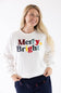 A smiling blonde woman wearing a white crewneck sweatshirt with colorful chenille "Merry & Bright" text across the chest, paired with dark blue lounge pants.