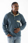 A man wearing a Patagonia fleece pullover in slate blue with beige contrast trim and a chest pocket, paired with blue jeans, against a plain white background.