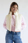 A woman modeling a cream-colored sleeveless puffer vest over a pink long-sleeve top and blue jeans, photographed against a plain light gray studio background.