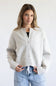 A woman modeling a light gray knit cardigan with a button-up front and drawstring detail, paired with light blue jeans against a plain white background.
