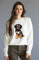 A woman wearing a white crewneck sweatshirt with a large embroidered dachshund graphic on the front, paired with olive green pants, set against a solid gray studio background.