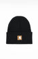 A black ribbed knit beanie hat with a folded cuff, featuring a small tan square patch on the front with the Carhartt logo, set against a plain white background.