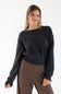 A woman modeling a dark charcoal gray knit sweater with a wide boat neckline and ribbed cuffs, paired with brown and beige striped pants, against a plain white studio background.