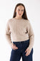A woman wearing a beige cable-knit crewneck sweater and dark blue jeans, standing against a plain white studio background.