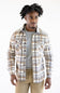 A man wearing a beige, brown, and gray plaid button-up flannel shirt over a gray t-shirt and khaki pants, photographed against a plain white studio background.