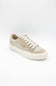 A low-top canvas sneaker in beige and off-white, featuring a patterned heel panel, white laces, and a thick white rubber sole, shown on a light gray background.