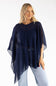 A woman modeling a sheer navy blue poncho-style top over a dark top and light blue jeans, photographed against a plain white studio background.