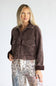 A woman modeling a dark brown corduroy jacket with front flap pockets, paired with patterned patchwork pants, against a light gray studio background.