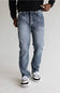 A person wearing light-wash blue denim jeans with a faded wash, paired with a black long-sleeve top and black-and-white sneakers, standing against a plain light gray studio background.