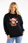 A woman wearing a black crewneck sweatshirt with a graphic of a Highland cow wearing a red Santa hat and holding a candy cane, paired with blue jeans, against a plain white background.