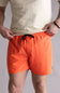 Front view of a person wearing orange bard shorts with a cream colored t-shirt on a neutral background. The shorts are the Quiksilver Everyday Solid Volley 15" Swim Shorts for Men in Hot Coral