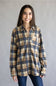 A woman wearing a long-sleeve button-up plaid shirt in beige, navy, and brown tones, paired with dark blue jeans, standing against a plain gray studio background.