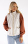 A woman wearing a two-tone fleece jacket with a cream body and rust-colored sleeves, paired with light blue jeans, against a plain white background.