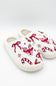 A pair of fuzzy white women's house slippers with embroidered festive holiday designs including a red reindeer, bow, candy canes, and snowflakes.