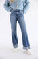 A person wearing light-wash blue distressed jeans with rolled cuffs, a light blue sweater, and white sneakers, photographed against a plain white studio background.