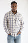 Front view of a man wearing the Hallstatt Knit Button Up Flannel Shirt in Sand with a plaid pattern in blue, beige, and gray, paired with light-wash jeans against a white backdrop.