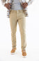 A person wearing slim-fit khaki pants, styled with a gray t-shirt, an open plaid flannel shirt, and tan sneakers, shown from the waist down on a white background.