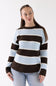 A woman wearing a knit sweater with horizontal stripes in light blue, off-white, and dark brown, paired with light-wash jeans, against a plain white studio background.