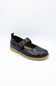 A single black leather Mary Jane shoe with a buckle strap and a tan sole, photographed on a white studio background.