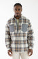 A man wearing a long-sleeve plaid flannel shirt with gray chest pockets, photographed against a plain white studio background.