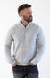 A man wearing a light gray marled quarter-zip knit sweater and dark jeans, standing against a plain white studio background.
