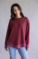 Woman wearing a maroon sweatshirt and blue jeans against a plain background