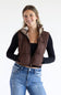 A smiling woman wearing a brown quilted puffer vest with a plaid-lined hood over a black long-sleeve top and blue jeans, photographed against a clean white studio background.
