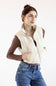 A woman wearing a cream-colored puffer vest over a brown long-sleeve top and blue jeans, posing against a plain white studio background.