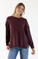 Image of a woman wearing a maroon colored slouchy sweater with blue denim jeans standing in front of a white studio background