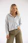 A woman modeling a light gray cable-knit zip-up hoodie sweater with a half-zip neckline and hood, paired with olive green pants, against a plain white studio background.