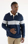 A man wearing a navy and grey color-blocked long-sleeve rugby shirt with blue jeans, standing against a plain light background.