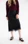 A model wearing a black midi skirt with a lace hem, paired with a burgundy knit sweater and black Mary Jane shoes, photographed against a plain white studio background.