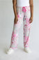 A person wearing a pair of pajama pants with a pink and white patchwork print, featuring a pink drawstring waist and white slippers, shown against a plain light gray background.