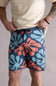 Front view of a person wearing blue shorts with orange and green abstract patterns on a plain background. The shorts are named Quiksilver Sol Tiles 19" Boardshorts for Men in Dark Denim.