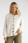 A blonde woman wearing a cream-colored knit cardigan sweater with brown buttons, paired with olive green pants, against a plain light gray background.