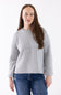 A woman wearing a light gray ribbed knit sweater and blue jeans, standing against a plain white studio background.