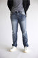 A person wearing light-to-medium wash blue jeans with a gray t-shirt, black jacket, and white sneakers, shown from the waist down against a plain light gray studio background.