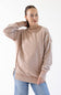 A woman modeling a light beige crewneck sweatshirt with long sleeves and side slits, paired with blue jeans, against a plain white background.