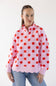 A woman wearing a pink long-sleeve quarter-zip pullover sweatshirt with a red polka dot pattern and a scalloped hem, paired with blue jeans, against a plain white background.