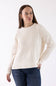 A woman wearing a cream-colored ribbed knit sweater and dark blue jeans, standing against a plain white studio background.