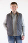 A male model wearing the FX Fusion Upland Quilted Field Vest in charcoal over a grey mock-neck quarter-zip sweater and blue jeans, standing against a neutral light background with his right hand in his pocket.