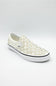 A white slip-on platform sneaker featuring a checkerboard pattern on the side and rows of silver metal studs across the toe box, shown against a light gray studio background.