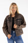 A woman modeling a dark brown washed denim jacket over a black top and blue jeans, photographed against a plain white studio background.