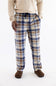 A person wearing plaid lounge pants in beige, blue, and brown, paired with a cream sweater and brown slippers, shown from the waist down on a white studio background.