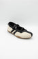 A single Mary Jane style shoe with a cream colored upper, black leather trim and strap, and a brown gum sole, shown against a plain light gray background.
