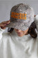 Camouflage cap with 'Midwest Princess' text worn by a woman in a gray sweatshirt.