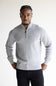 A man wearing a light gray ribbed knit quarter-zip pullover sweater and dark trousers, standing against a plain light background.