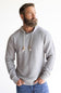 A man with a full beard wearing a light gray waffle-knit hoodie with white drawstrings, paired with blue jeans, standing against a plain white background.